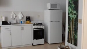 Pieni, käytännöllinen keittiö, jossa on valkoiset kaapit, liesi, mikroaaltouuni ja jääkaappi.