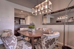 A dining area with a wooden table, four upholstered chairs with a spotted pattern, and a modern pendant light fixture above.