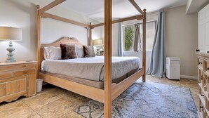 Una cama con dosel sobre un marco de madera, una mesita de noche con lámpara y un aparador con cajones.