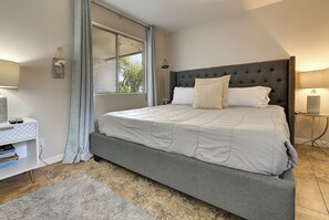 A bedroom with a large bed, a bedside table, a lamp, and a window with curtains.