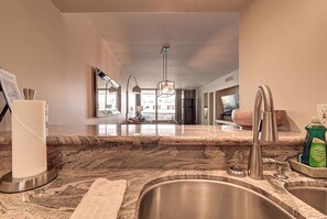 A modern kitchen with granite countertops, stainless steel sink, and a hanging light fixture.