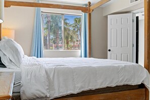 A single bed with a wooden headboard, a window with blue curtains, and a white door.