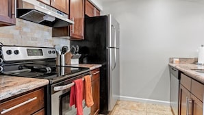 Una cocina con armarios de madera, un refrigerador de acero inoxidable, un horno negro y una encimera de granito.