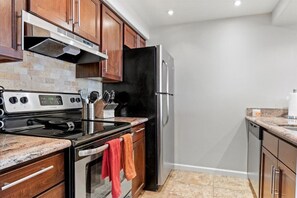 A kitchen with wooden cabinets, a stainless steel refrigerator, a black oven, and a granite countertop.