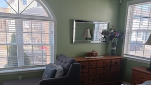 Ein Schlafzimmer mit Bett, Sofa, Kommode und einem großen Fenster mit Jalousien.