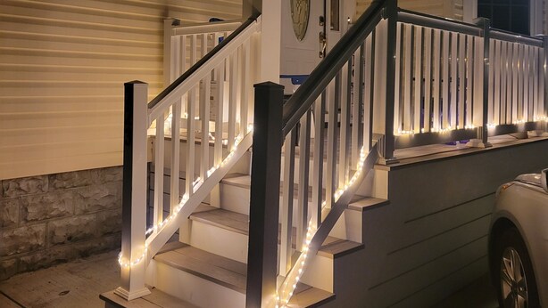 Ein Haus mit einer Veranda, einer Treppe mit weißen Geländern und einem geparkten Auto davor.