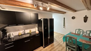 A compact kitchen with dark cabinets, a black refrigerator, and a dining area with a teal tablecloth and green chairs. - Idyllischer Bauernhof 3 (Wildensbuch)