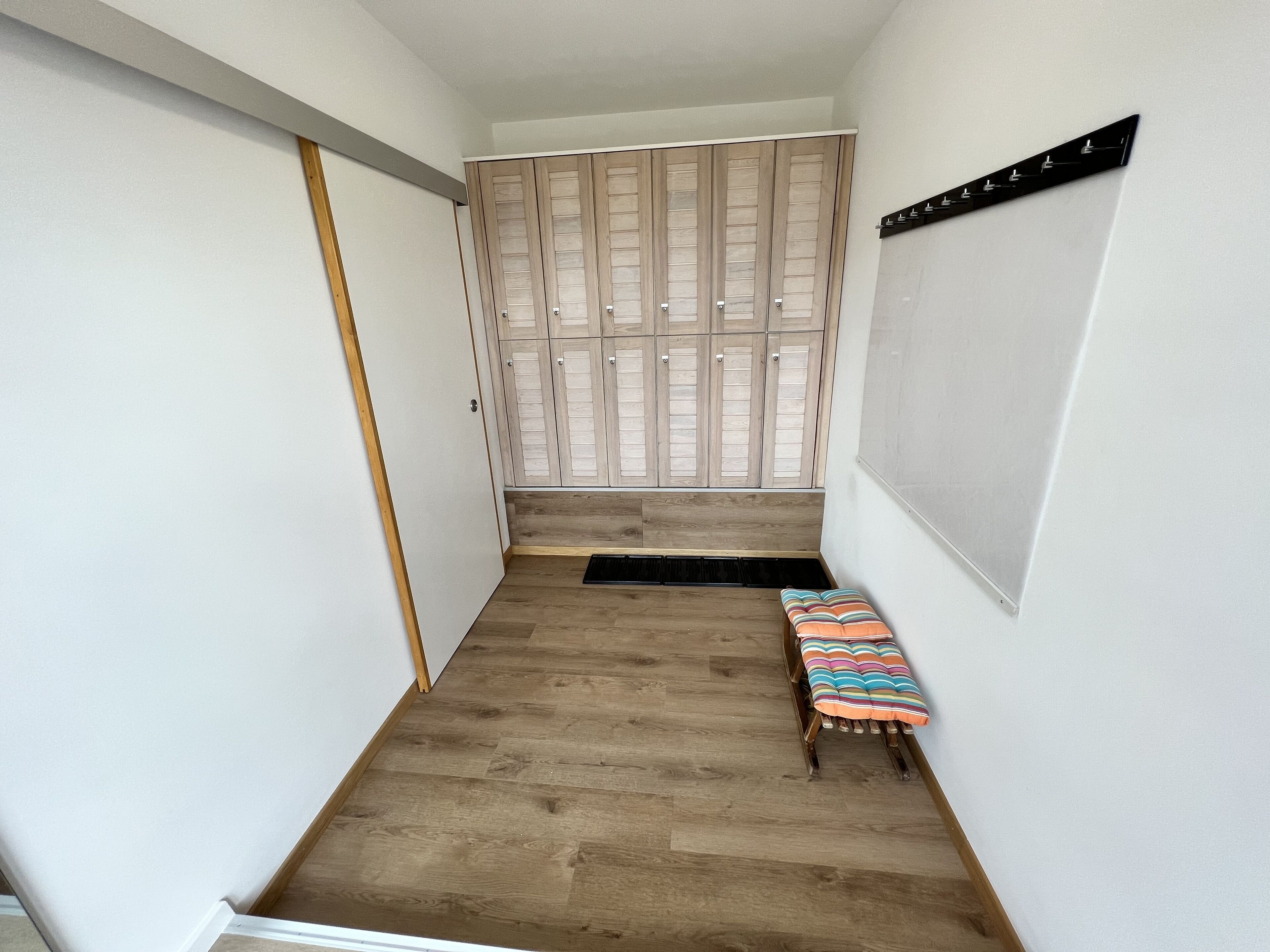 A narrow hallway with wooden flooring, a bench with a striped cushion, and a set of wooden doors at the end.
