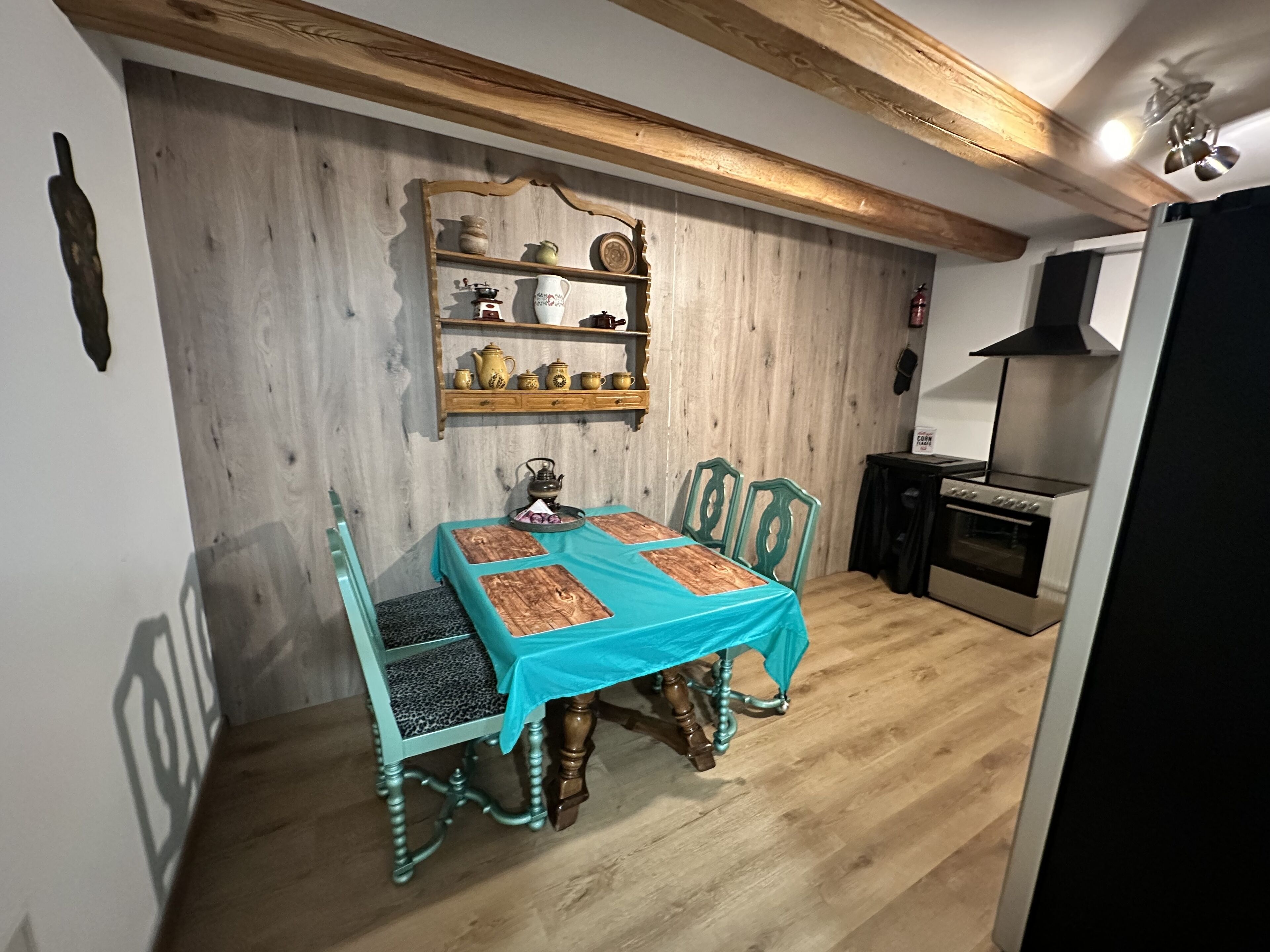 Zona pranzo con tavolo e sedie in legno, mensola con stoviglie e cucina moderna con piano cottura e forno.