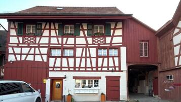 Ein traditionelles Fachwerkhäuschen mit einer Garage, einem kleinen Laden im Erdgeschoss und einem geparkten Auto davor.