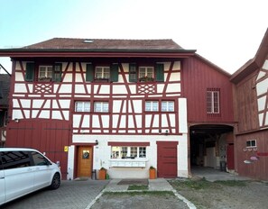 Ein traditionelles Fachwerkhäuschen mit einer Garage, einem kleinen Laden im Erdgeschoss und einem geparkten Auto davor.