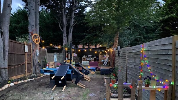 Ein Garten mit Holzzaun, Rutsche und Lichterkette.