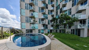 A modern apartment building with a swimming pool, wooden deck, and green lawn.
