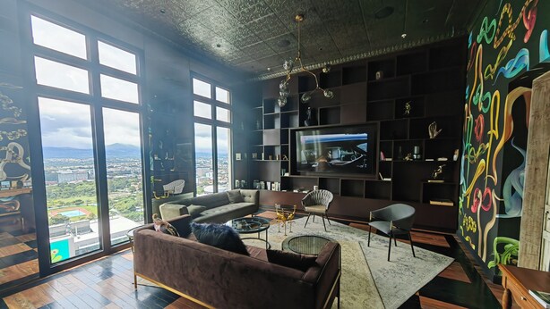 A modern living room with a large TV, a sofa, and a view of a cityscape through large windows.