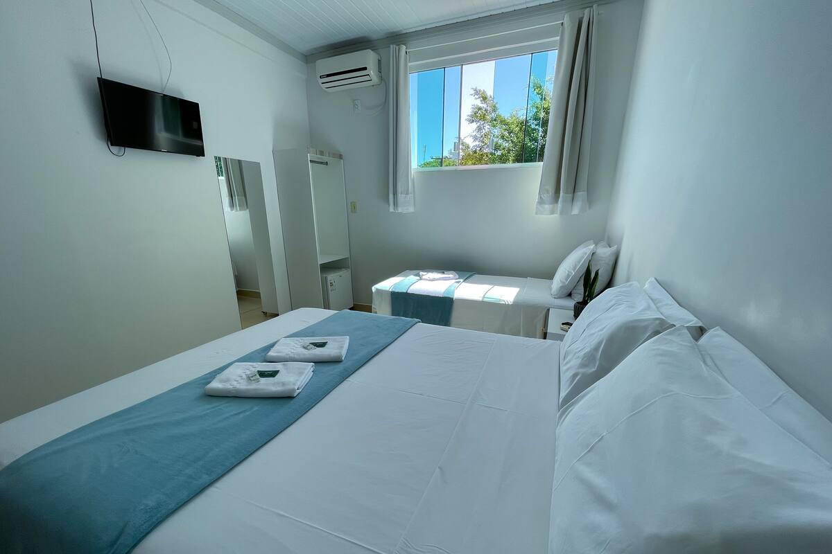 A hotel room with a large bed, a smaller bed, a TV mounted on the wall, and a window with curtains.