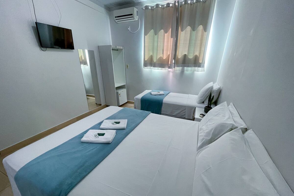 A hotel room with two beds, a TV, an air conditioner, and a window with curtains.