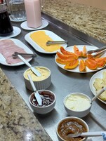 Una mesa de bufé con diversos alimentos, entre ellos jamón en rodajas, queso, papaya y varias opciones de salsas y untables en recipientes pequeños.