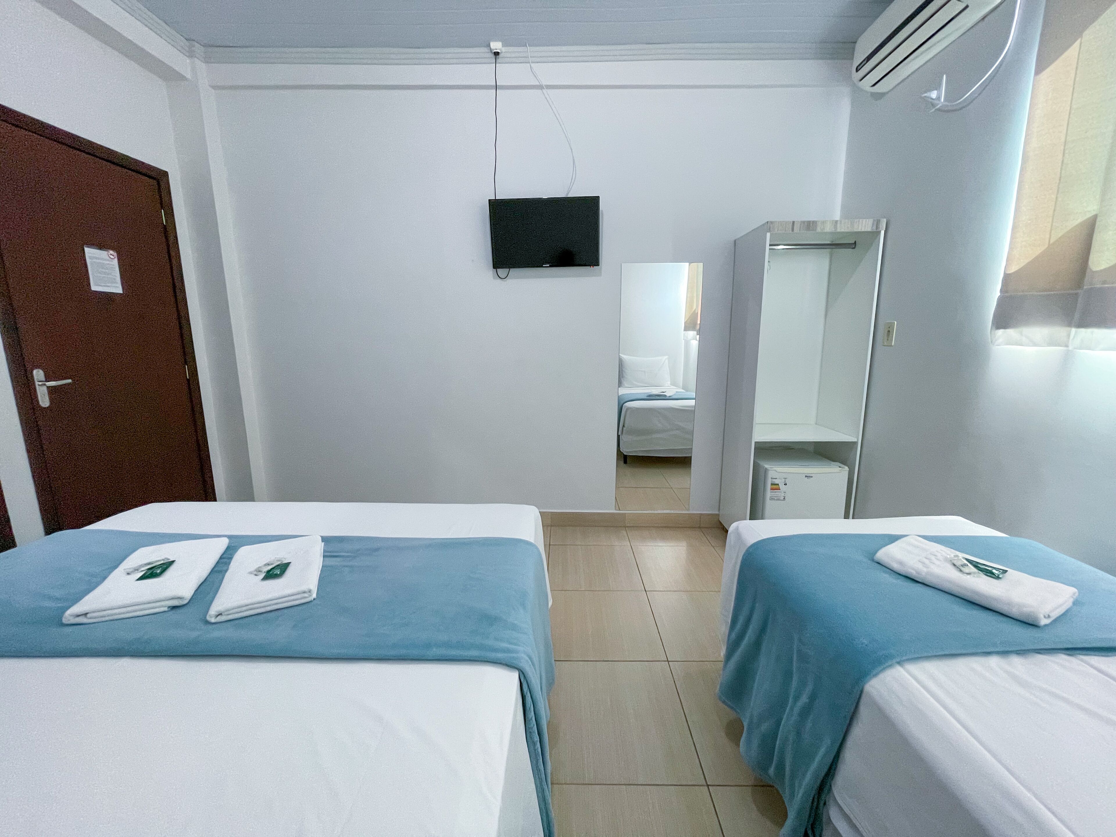 A hotel room with two beds, a TV, a wardrobe, and a bathroom visible through an open door.