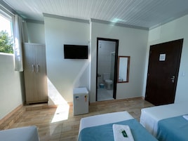 Habitación de hotel con dos camas, televisión, refrigerador, armario y baño visible a través de una puerta abierta.