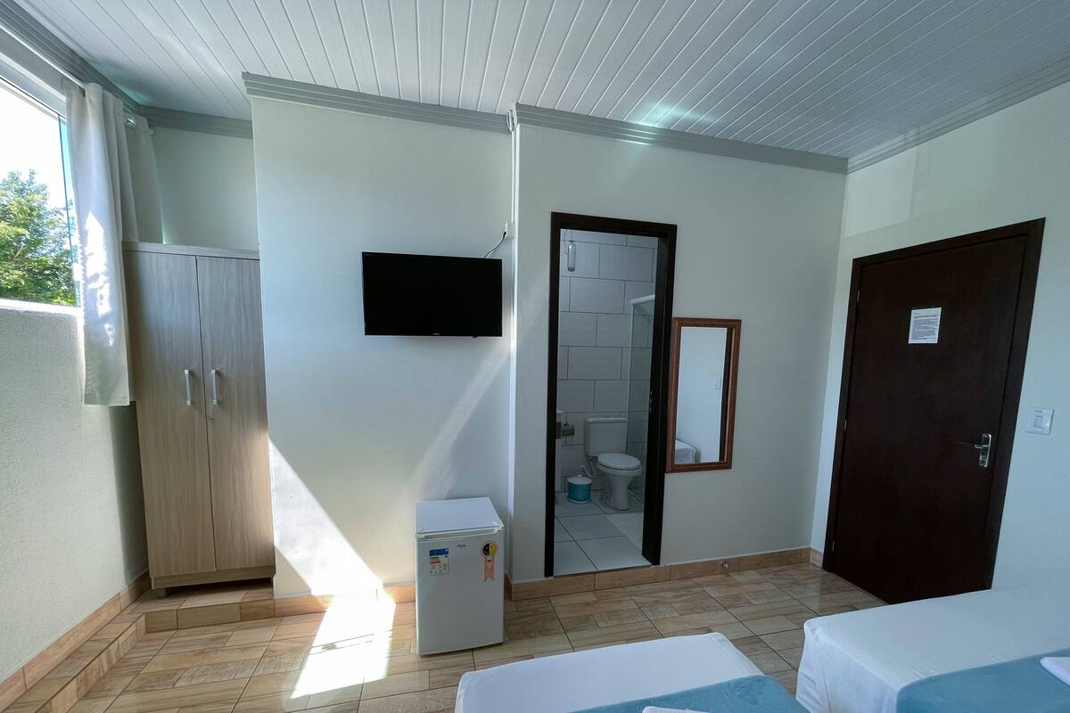 A hotel room with two beds, a TV, a refrigerator, and a bathroom visible through an open door.