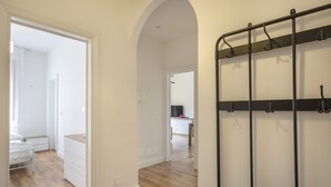 Un couloir avec un porte-manteau, un lit et, au fond, un coin cuisine.