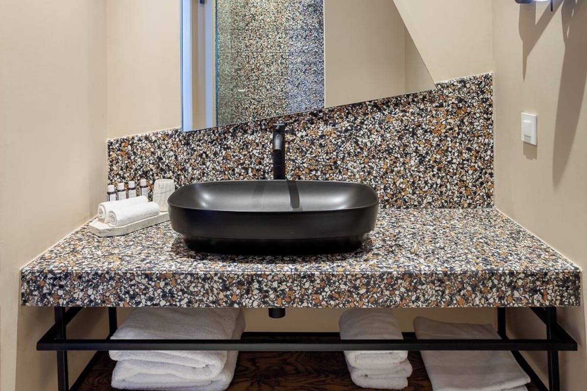 A modern bathroom with a black sink, a speckled countertop, and a mirror with a light.