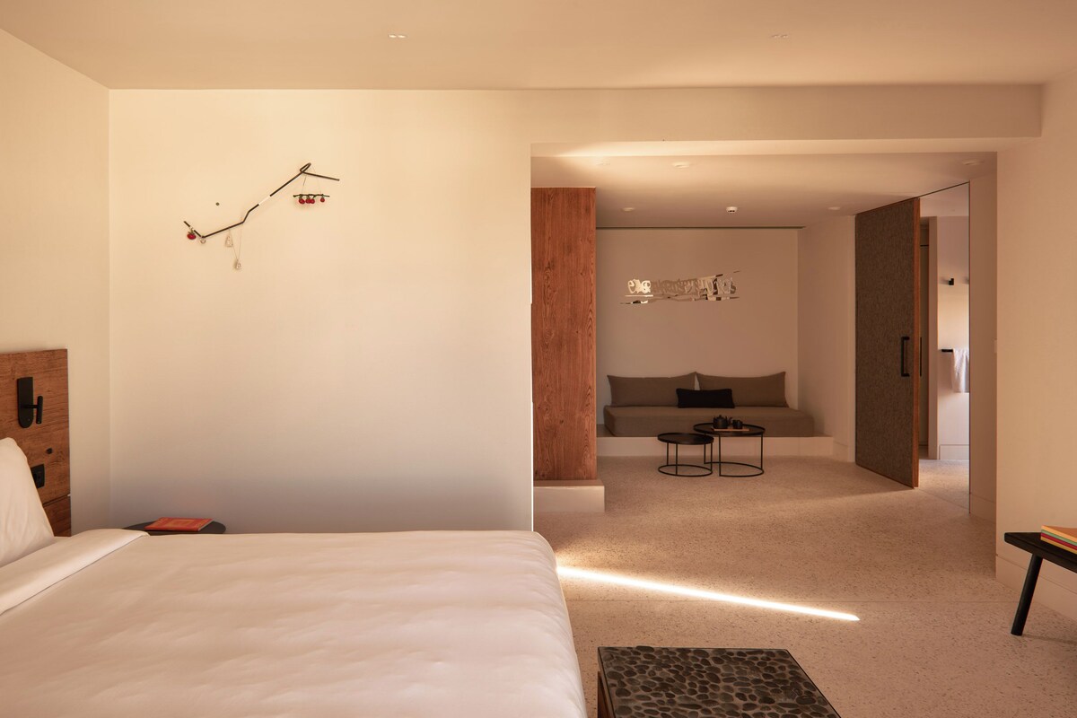 A modern hotel room with a large bed, a small table, and a seating area with a sofa and a coffee table.