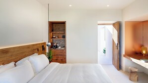 A modern bedroom with a large bed, wooden headboard, built-in shelving, and a small desk area. - Nous Santorini (Santorini)