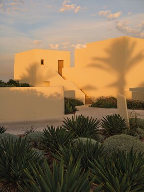 A modern building with a flat facade, a central staircase, and a garden with agave plants. - Nous Santorini (Santorini)