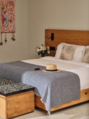 Una cama bien hecha con cabecera de madera, una manta azul y un sombrero de paja sobre la cama.