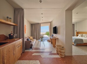 Habitación de hotel moderna con sofá, mesa de comedor, cama, televisor y vistas al exterior.