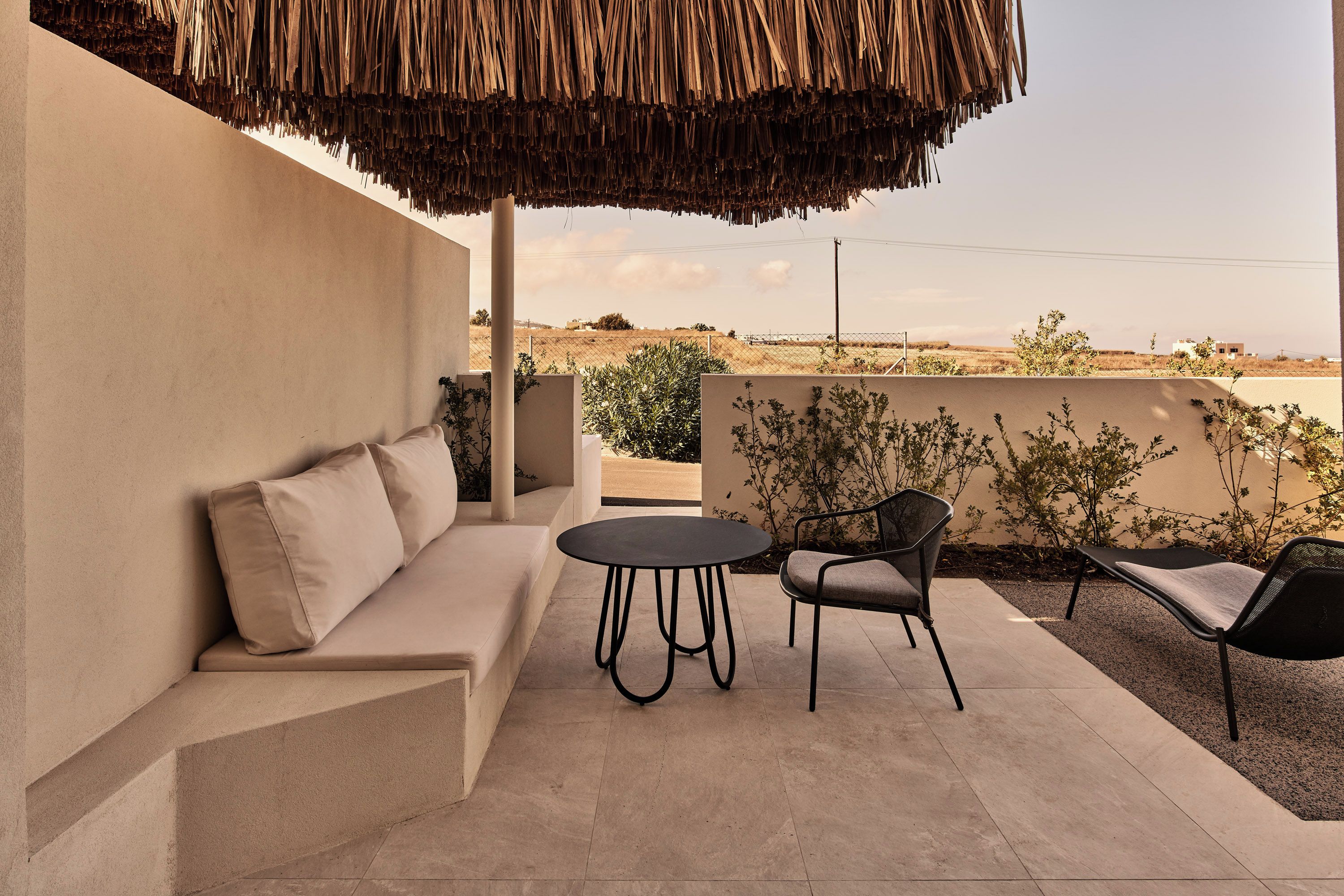 A patio with a sofa, two chairs, a round table, and a thatched roof.