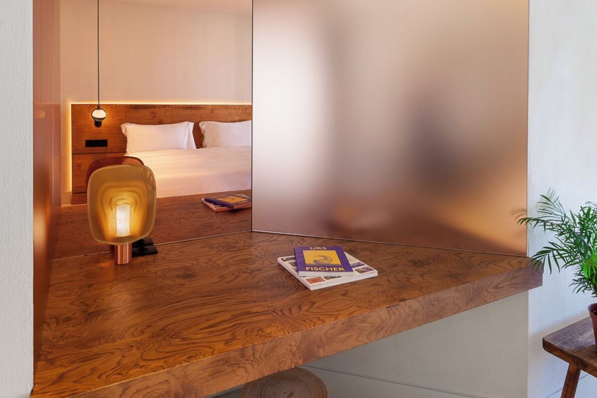 A modern hotel room with a wooden desk, a bedside lamp, and a bed with white linens.