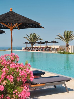 A poolside area with lounge chairs and umbrellas, a clear sky, and a view of the sea. - Nous Santorini (Santorini)