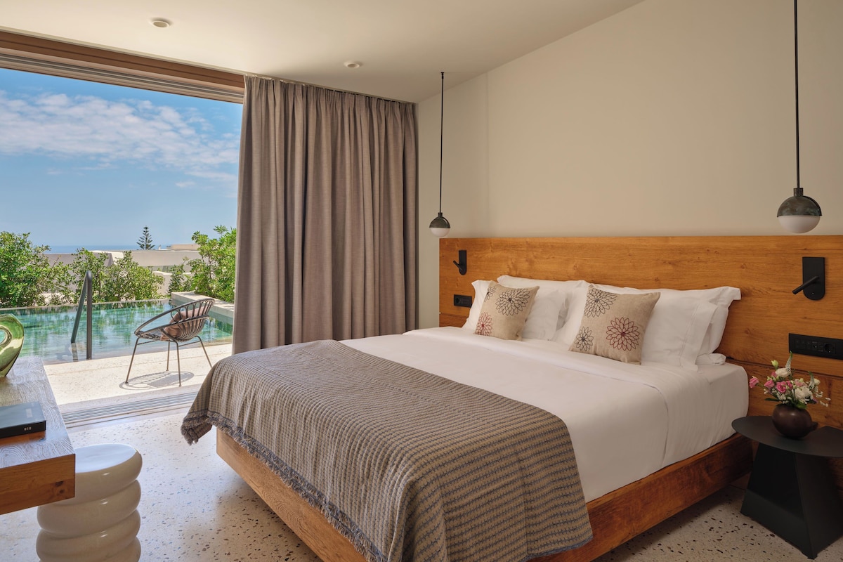 A bedroom with a large bed, a view of the ocean, and a balcony with a chair.