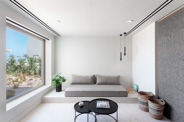 A modern room with a large window, a sofa, a small table, and a plant. - Nous Santorini (Santorini)