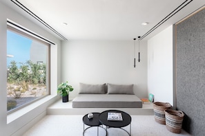 A modern room with a large window, a sofa, two small tables, and a plant. - Nous Santorini (Santorini)