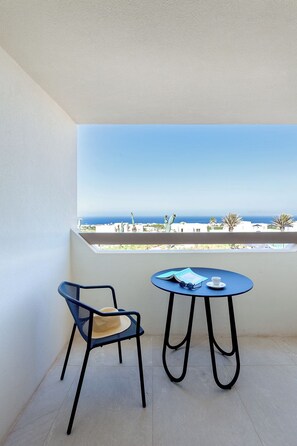 A balcony with a table and chair, a view of the sea, and a clear sky.