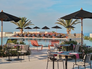 A poolside area with lounge chairs, umbrellas, and dining tables. - Nous Santorini (Santorini)