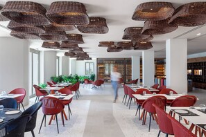 A modern restaurant with wicker ceiling lamps, red and black chairs, and a central walkway. - Nous Santorini (Santorini)