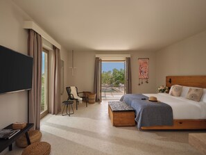 A bedroom with a large bed, a flat-screen TV, a chair, a small table, and a view of the outdoors. - Nous Santorini (Santorini)