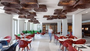 A modern restaurant with wicker ceiling lamps, red and black chairs, and a central walkway. - Nous Santorini (Santorini)