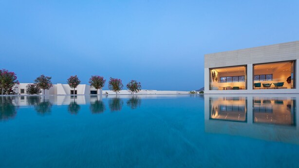 A modern building with large windows, an infinity pool, and a clear blue sky. - Nous Santorini (Santorini)