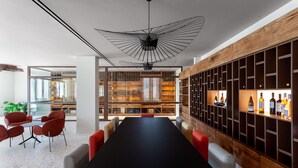 A modern conference room with a long table, red chairs, a wooden bookshelf with wine bottles, and a unique ceiling light fixture. - Nous Santorini (Santorini)