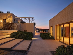 A modern building with a pathway leading to a seating area, surrounded by greenery. - Nous Santorini (Santorini)