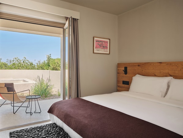 A hotel room with a bed, a small table, a chair, a window with curtains, and a picture on the wall. - Nous Santorini (Santorini)
