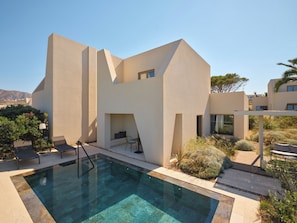 A modern building with a pool, outdoor seating, and a view of the landscape. - Nous Santorini (Santorini)