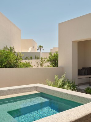 A pool area with a clear blue pool, surrounded by low walls and greenery. - Nous Santorini (Santorini)