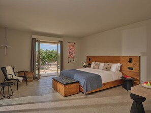 A bedroom with a wooden bed, a small table, a chair, and a view through a glass door. - Nous Santorini (Santorini)
