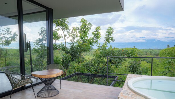 Une terrasse extérieure moderne, dotée d’une table et de chaises en bois, d’un jacuzzi et offrant une vue imprenable sur un paysage luxuriant.